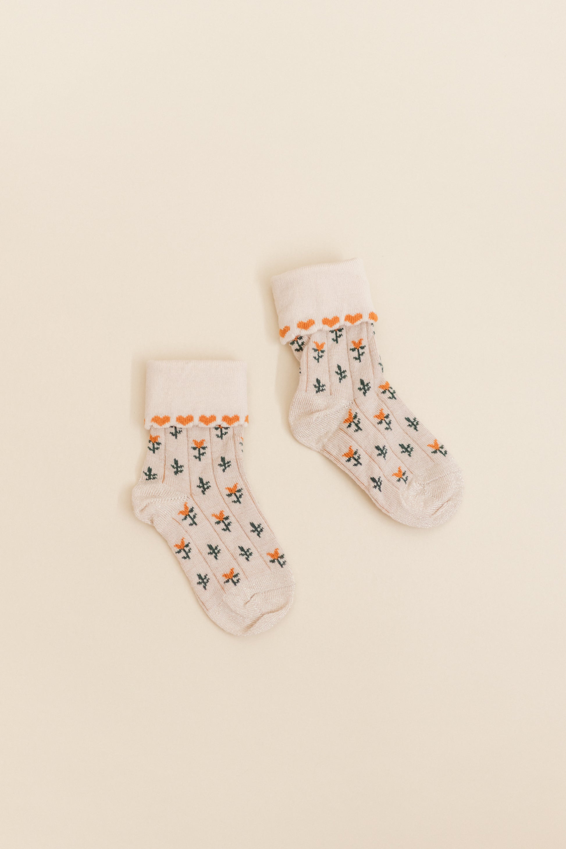 Close-up of Kennedy socks in Spice by Shop Little Millers, showing a cream-colored knit fabric with dainty floral accents and fine heart-style trim, soft ribbed cuff, and flexible stretch designed to keep baby and children’s feet comfortable while playing or dressing up.