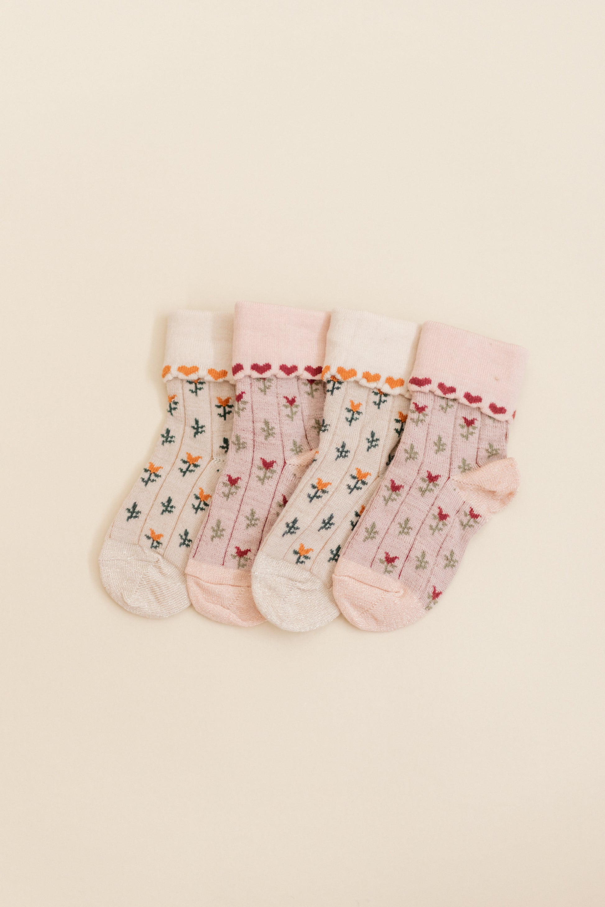 Close-up of Kennedy socks displayed side by side to capture the details of the socks by Shop Little Millers, showing a cream-colored knit fabric with dainty floral accents and fine heart-style trim, soft ribbed cuff, and flexible stretch designed to keep baby and children’s feet comfortable while playing or dressing up.